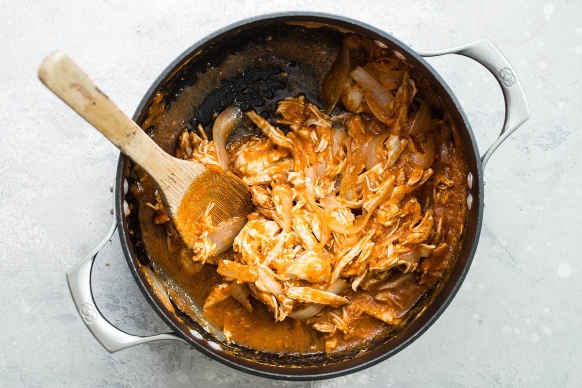 Tinga sauce being stirred in to a saucepan with chicken.