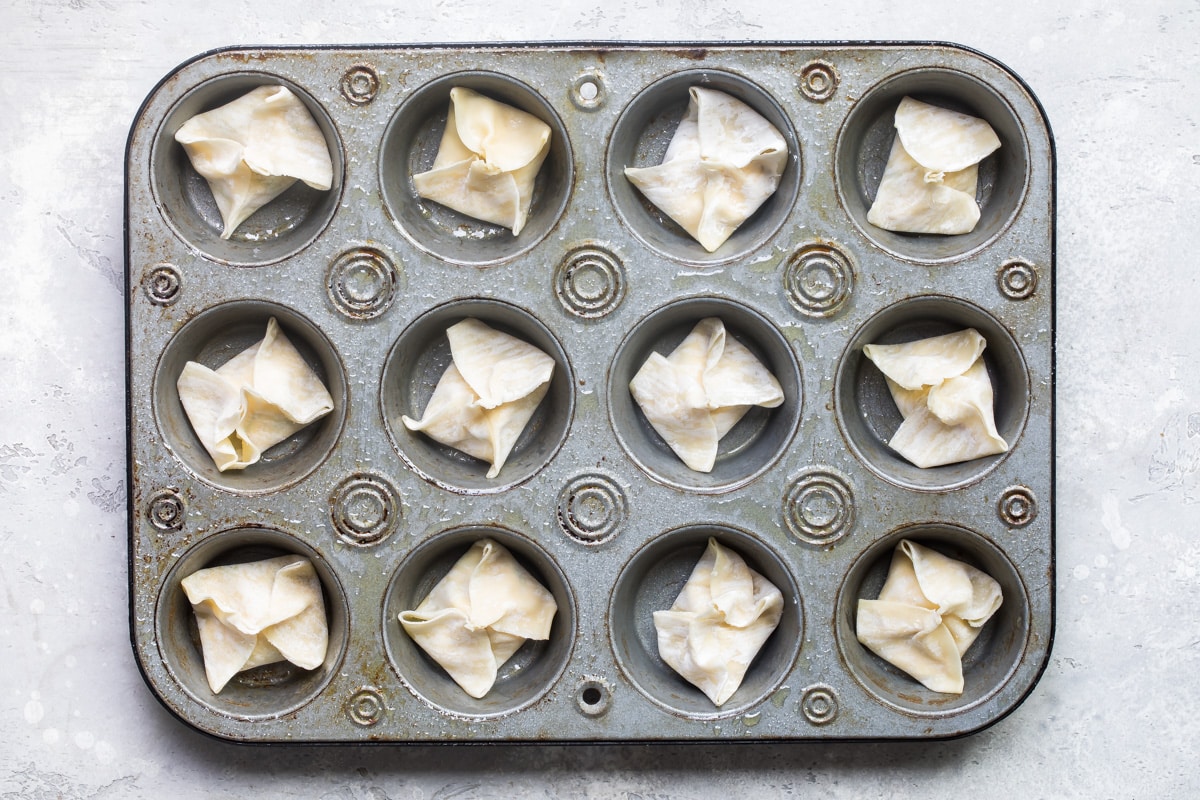 Cream cheese wontons in a muffin pan before being baked.