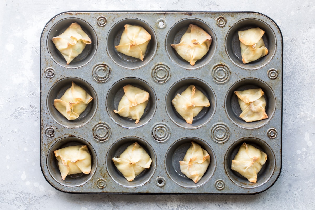 Twelve cheese wontons in a muffin tin after being baked.