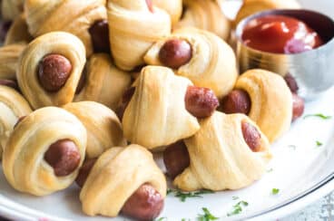 Easy pigs in a blanket on a white plate with a side of ketchup.