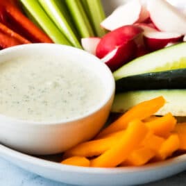 A small bowl of green goddess dressing surrounded by raw vegetables.