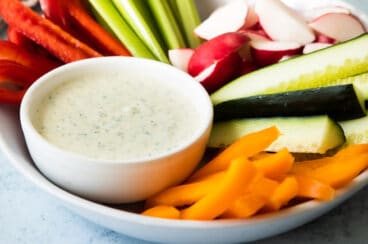 A small bowl of green goddess dressing surrounded by raw vegetables.