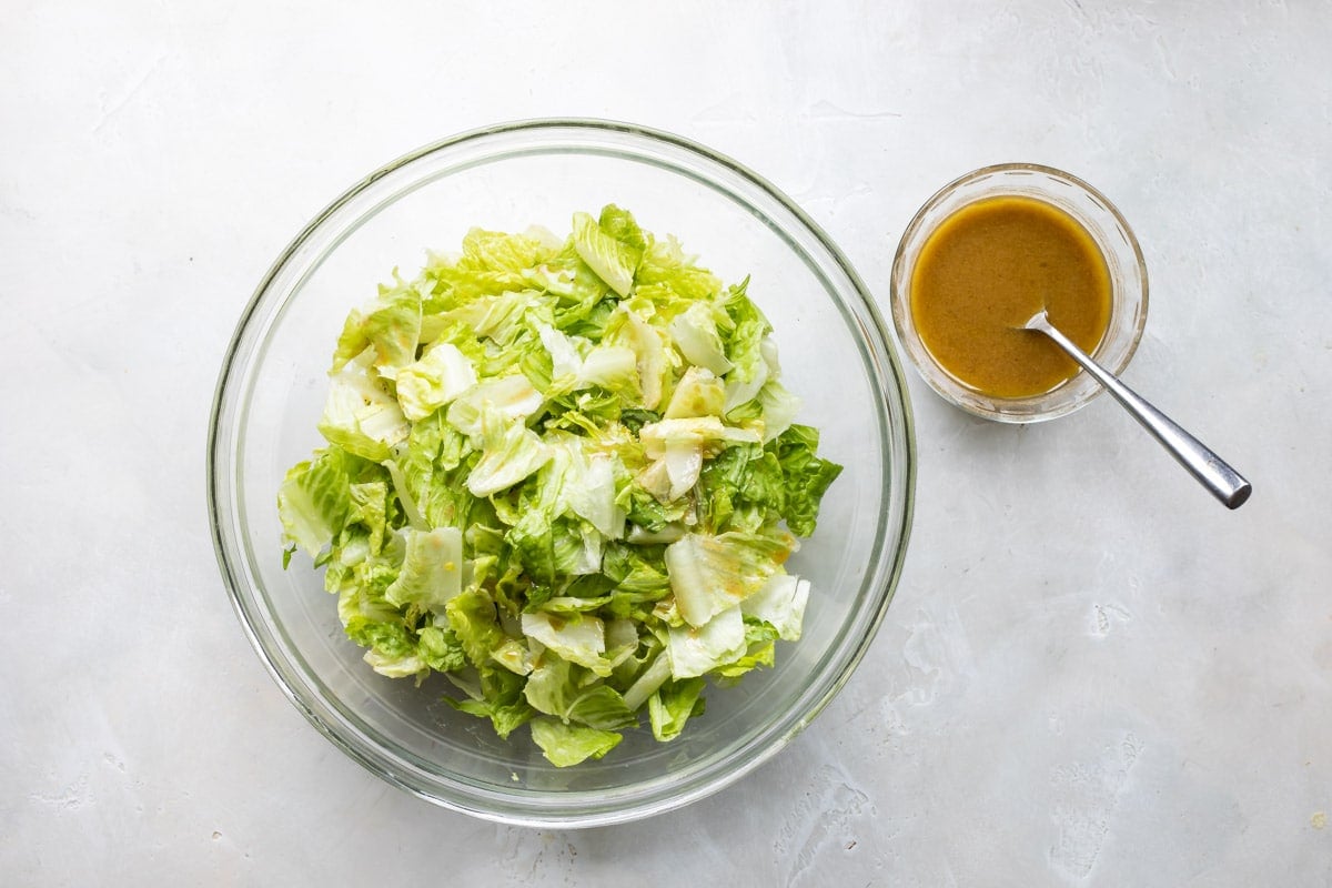 A bowl of lettuce with mustard vinaigrette nearby.
