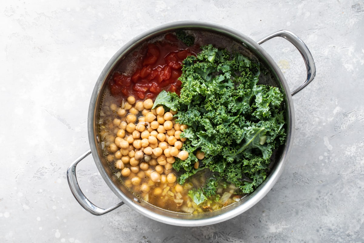 Adding chickpeas, kale, and tomatoes to Minestrone soup.