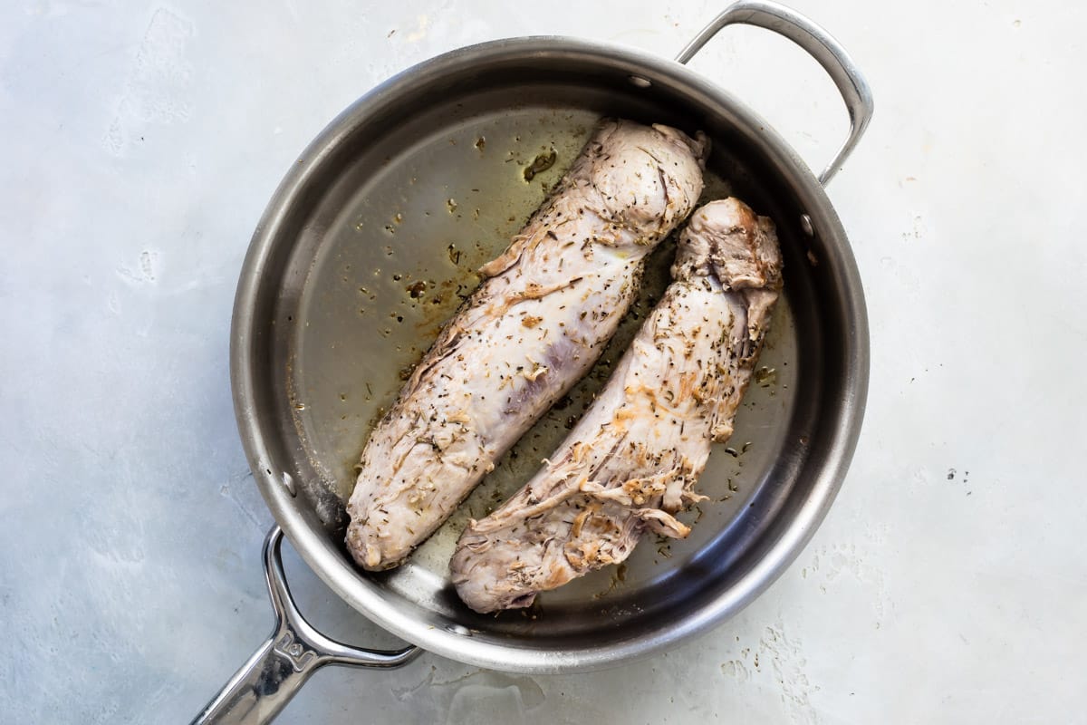 Pork tenderloin being cooked in a silver skillet.