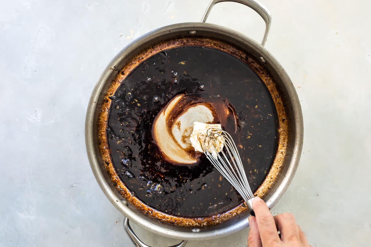 Someone mixing balsamic glaze in a metal skillet.