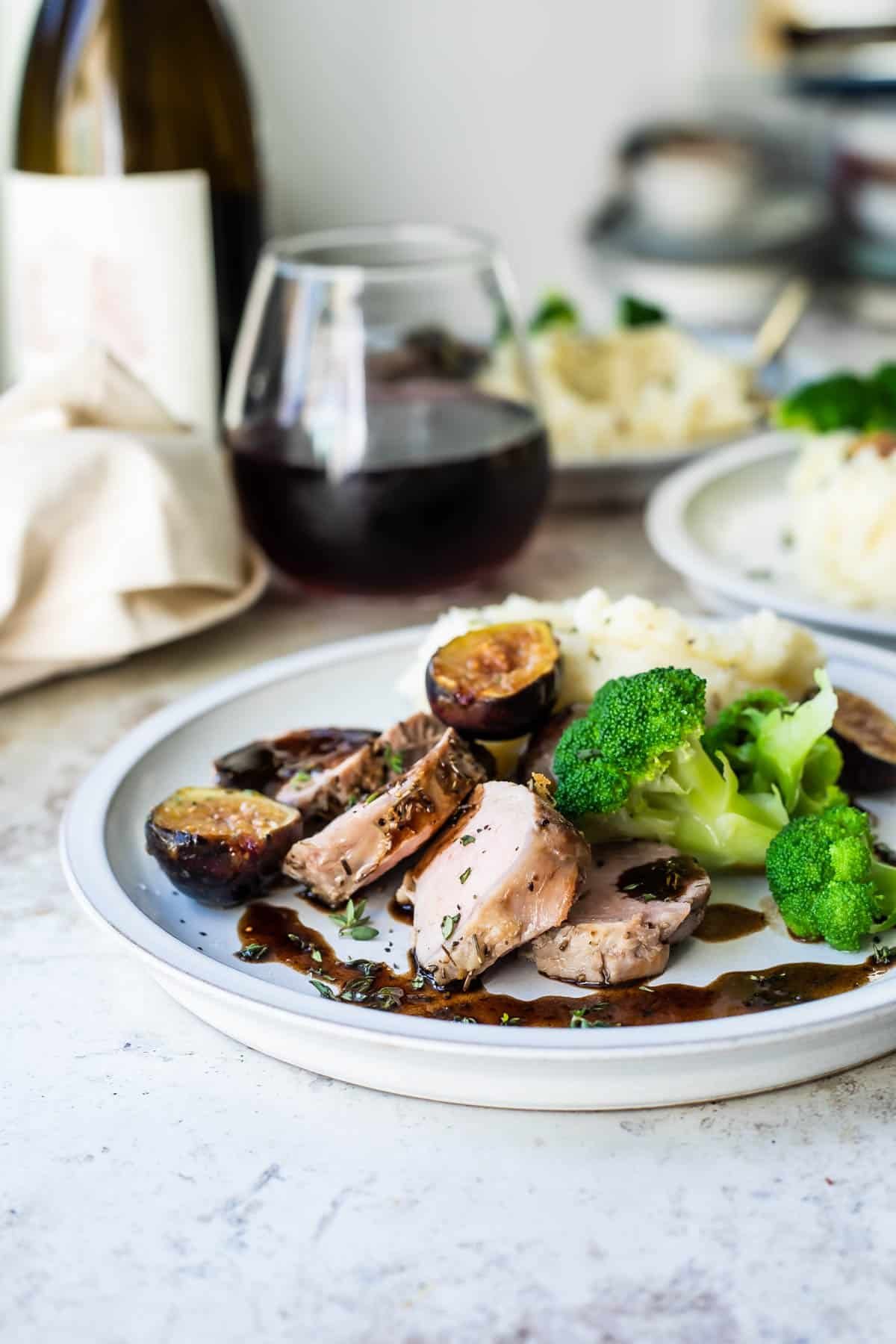 A plate with mashed potatoes, broccoli and pork tenderloin with figs.