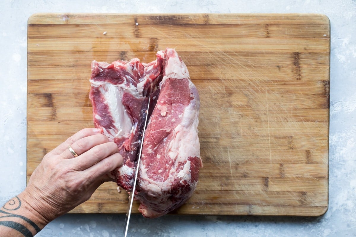 Raw prime rib being sliced on a wooden cutting board.