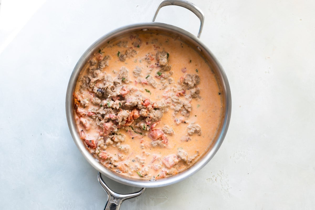 A skillet of sausage with tomato cream sauce.