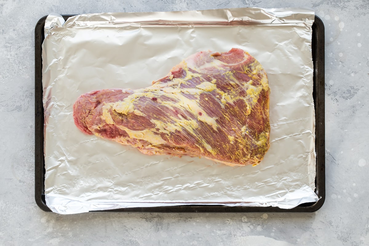 Tri tip with mustard rubbed on it on a foil covered baking sheet.