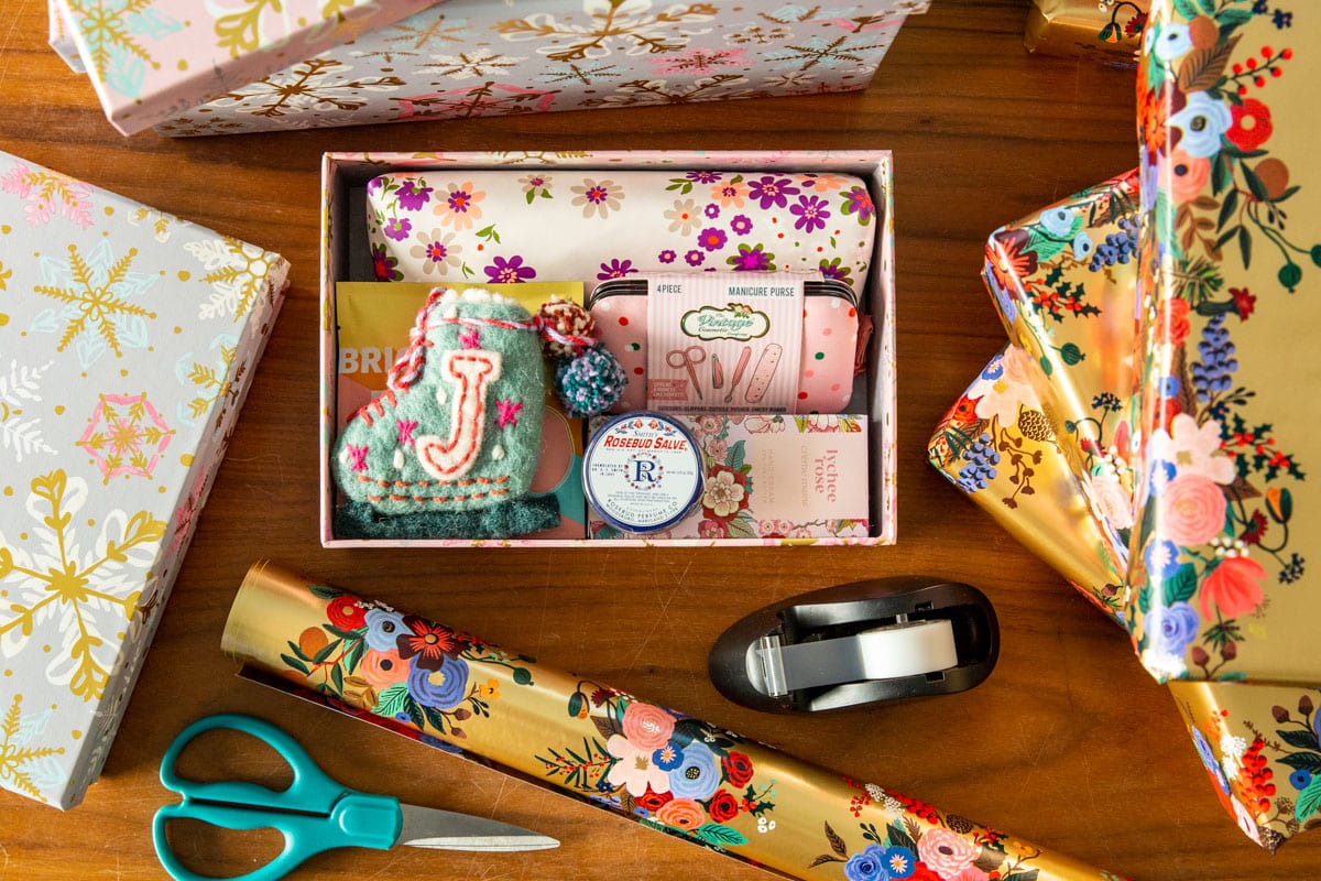 A holiday box filled with presents with wrapping paper nearby.