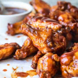 Air fryer chicken wings covered in barbecue sauce on a wooden cutting board.