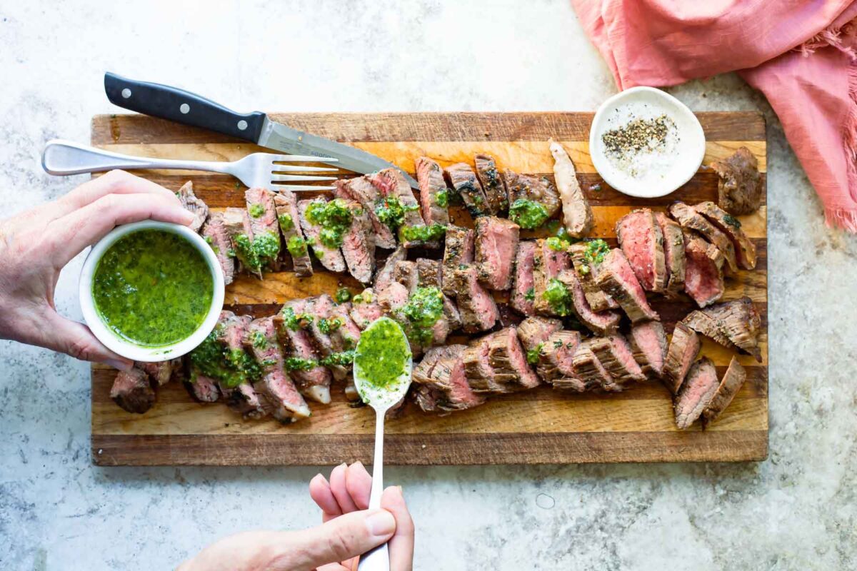 Someone spooning Chimichurri sauce over steak pieces.