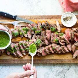 Someone spooning Chimichurri sauce over steak pieces.