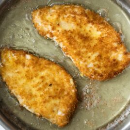 Chicken being breaded in a silver skillet.