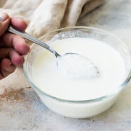 Someone scooping a spoonful of buttermilk out of a small glass bowl.