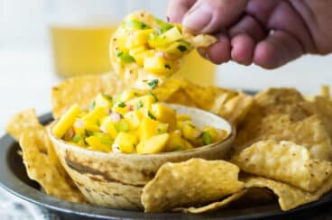 Someone scooping mango salsa out of a bowl with a chip.