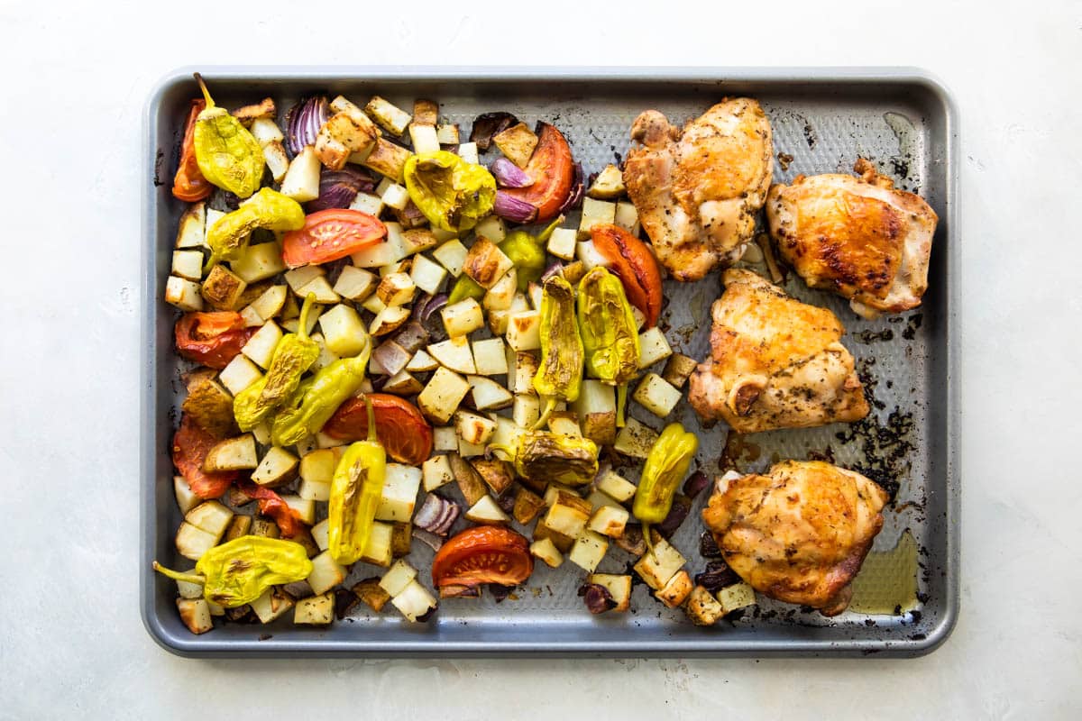 Greek chicken on a baking sheet with vegetables.