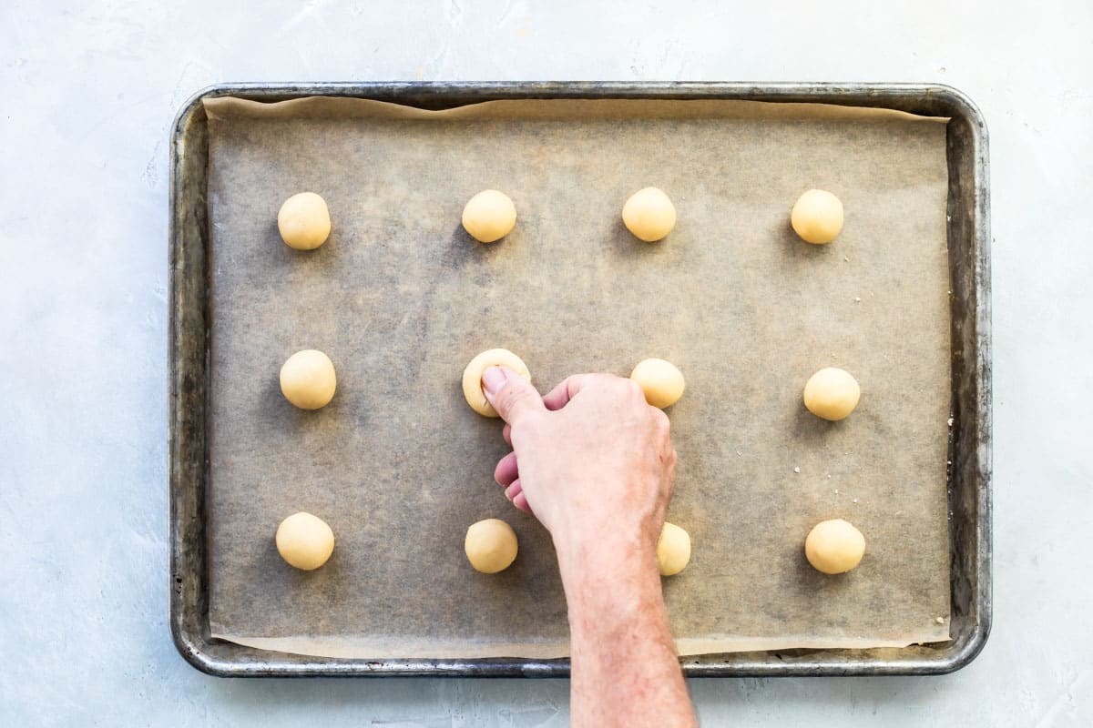 Pressing a thumb into cookie dough to make thumbprint cookies.