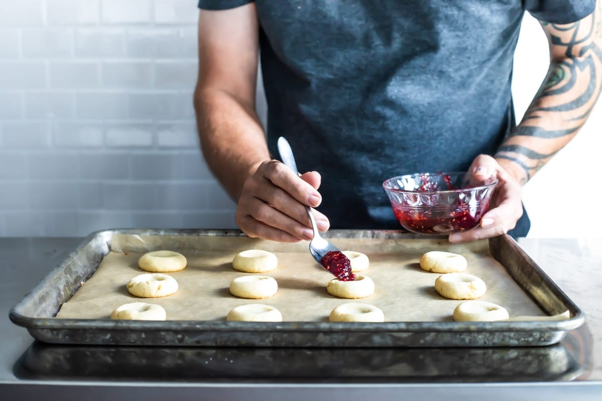 Spooning jelly into thumbprint cookies.