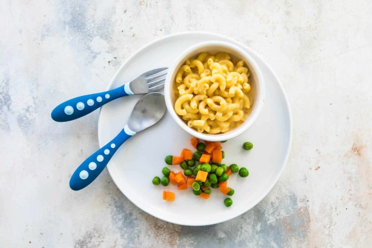 A toddler lunch of macaroni and cheese with a side of peas and carrots.