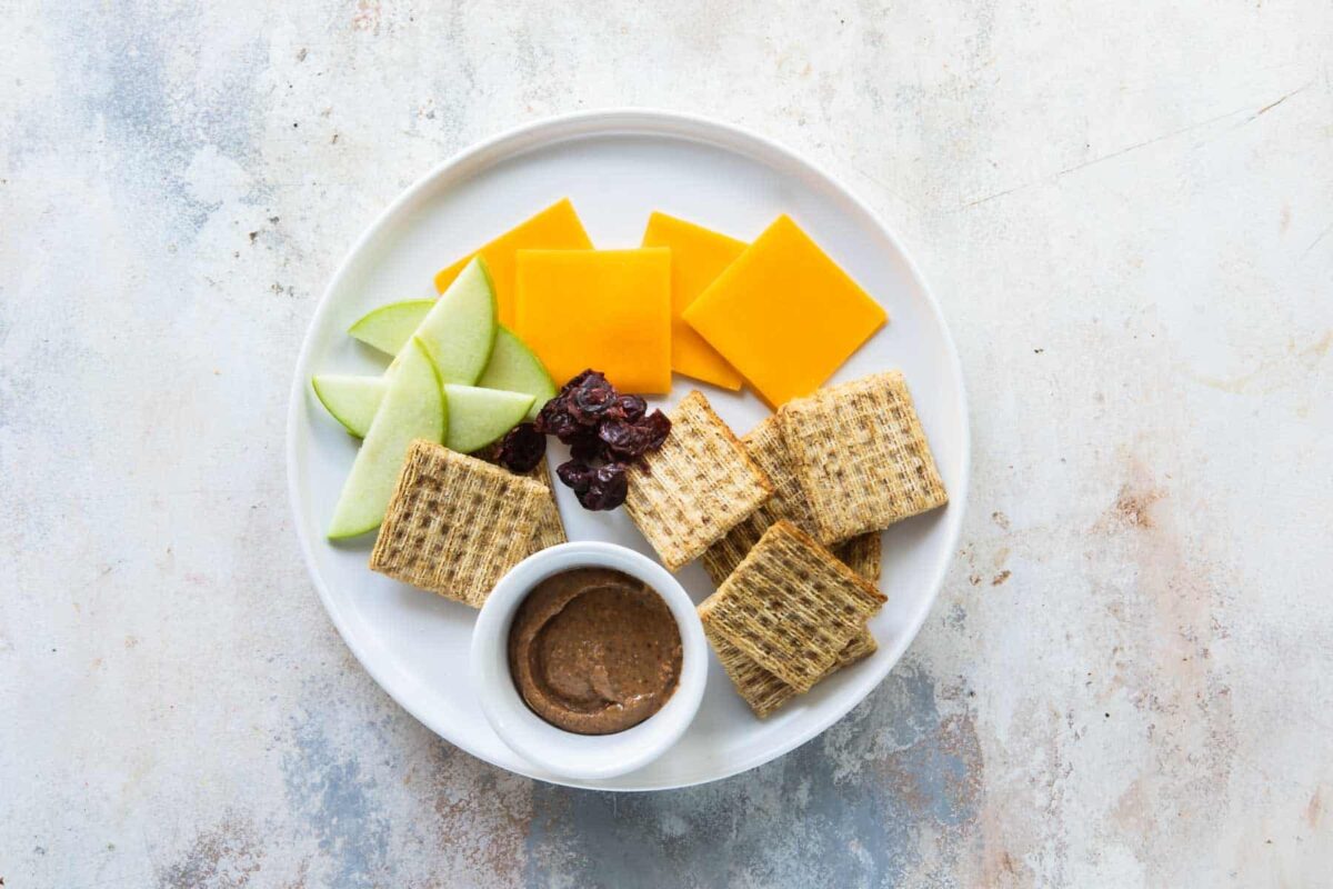 A toddler lunch of crackers, sunflower seed butter, cheese and apples.