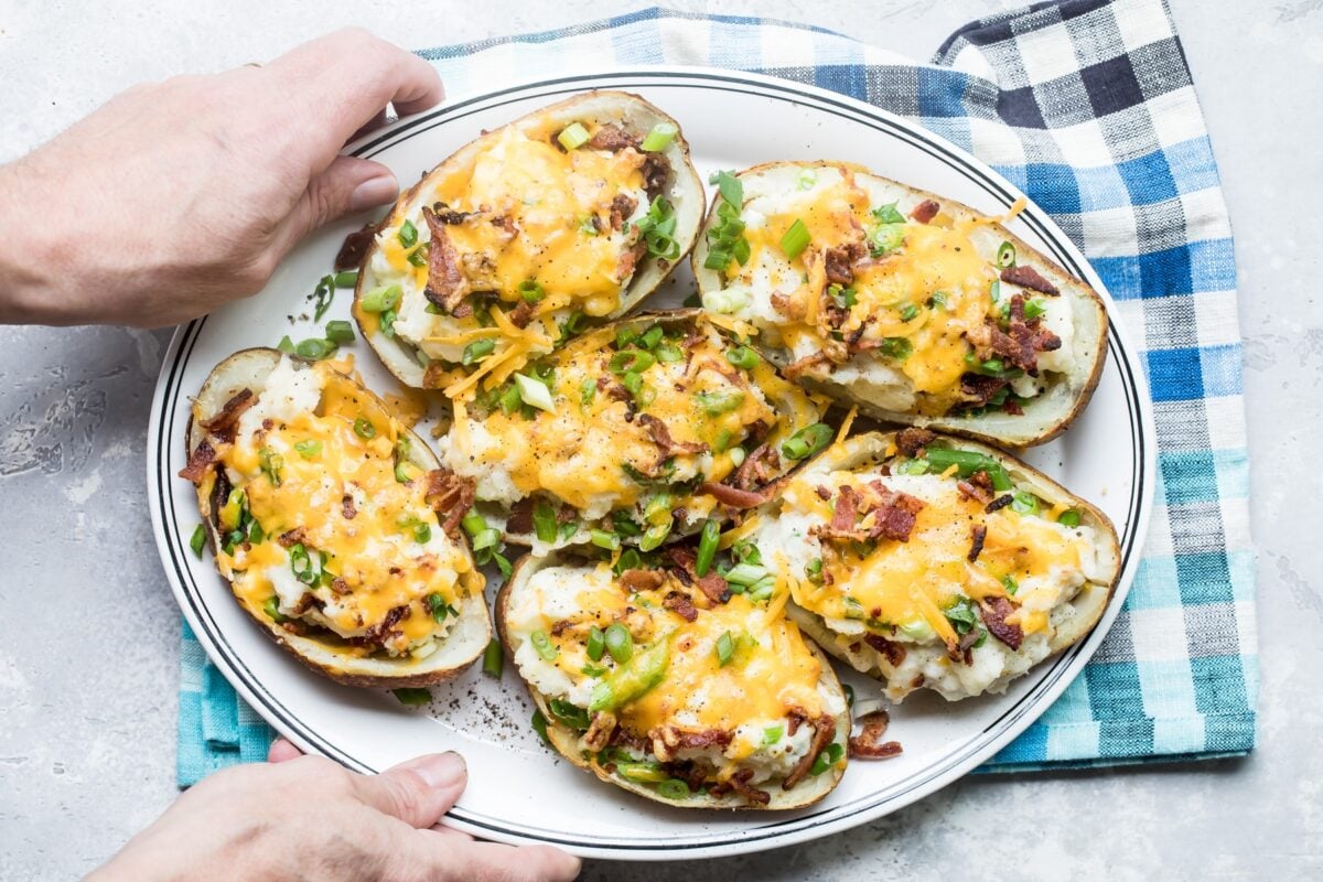 Someone holding a plate with twice baked potatoes on it.