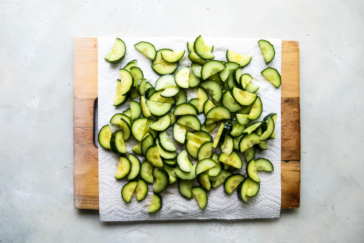 Cucumber slices resting on a paper towel lined cutting board.