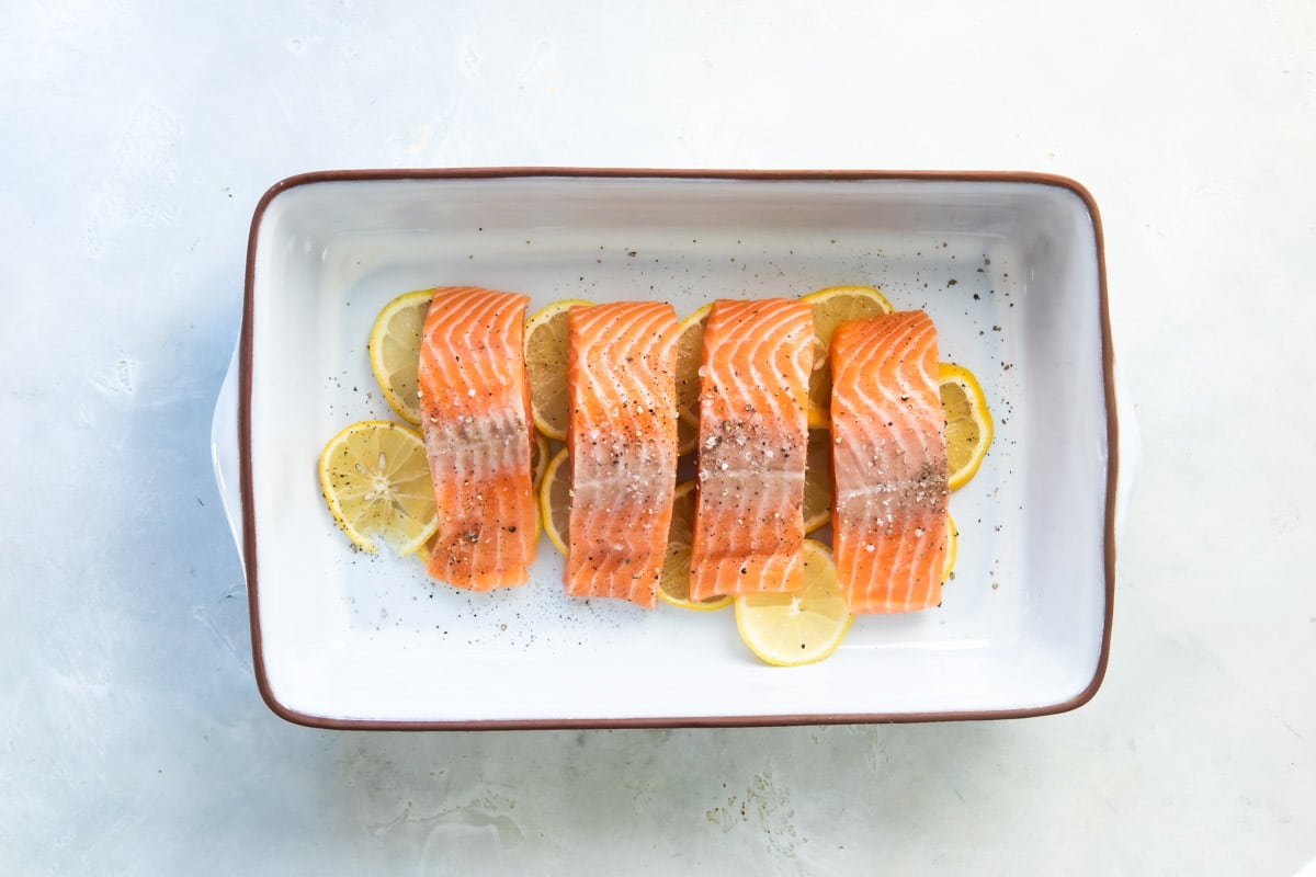 Salmon filets on top of lemon slices in a white baking dish.