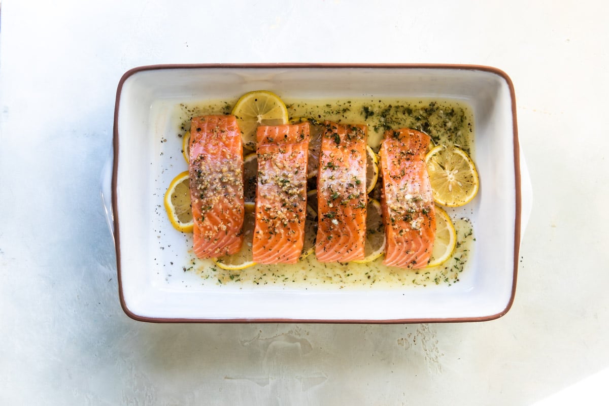 Raw salmon filets over a bed of lemon slices in a white baking dish.