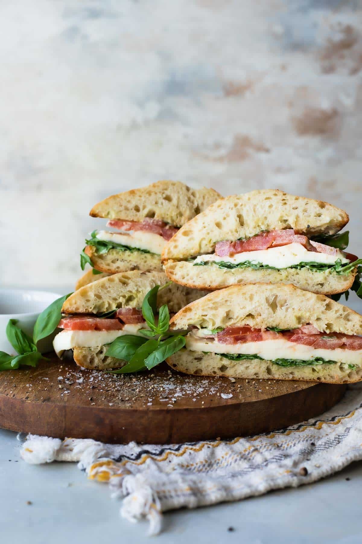 A stack of caprese sandwiches on a wooden cutting board.