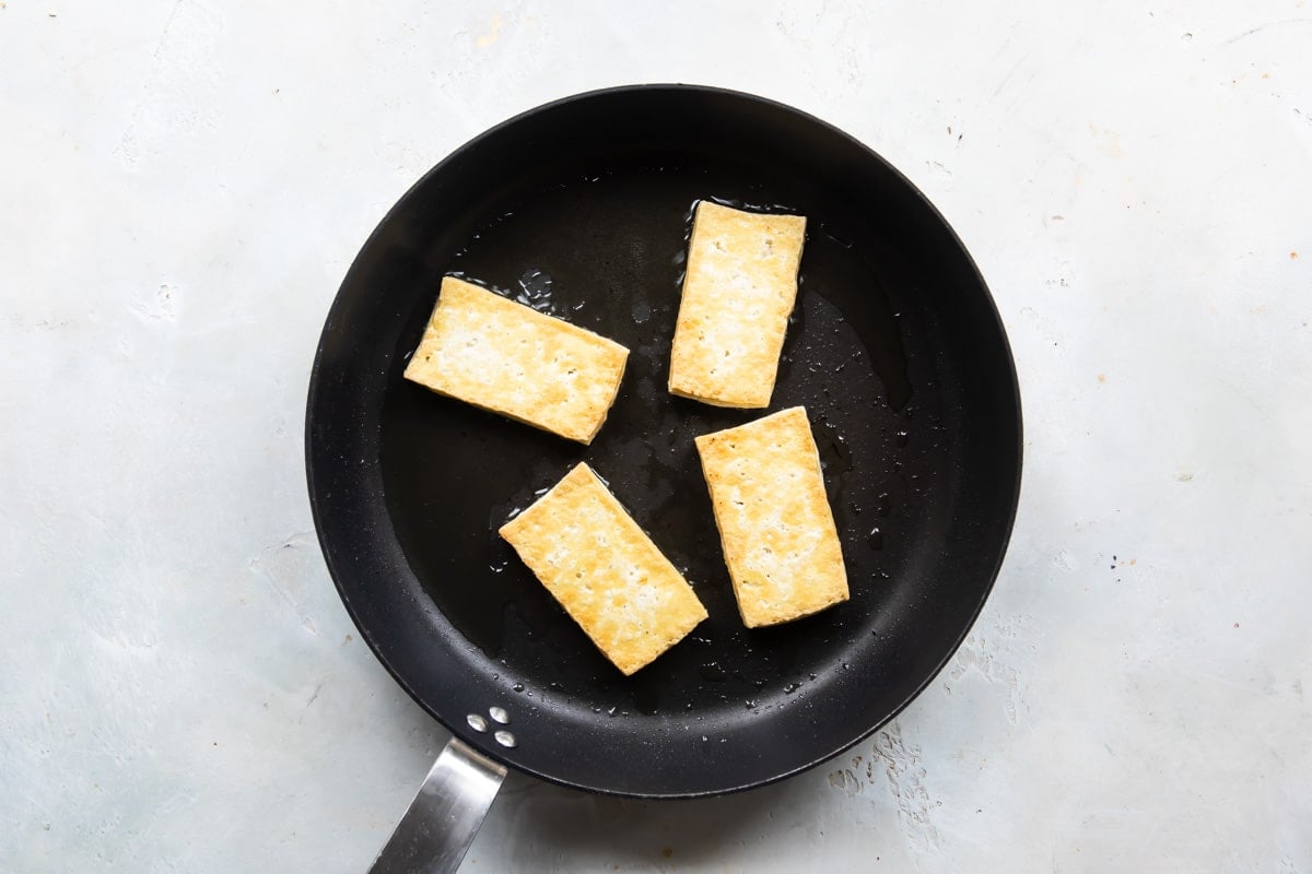 Tofu slices being cooked in a frying pan.