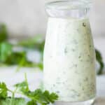 Creamy cilantro lime dressing in a tapered glass open top bottle.