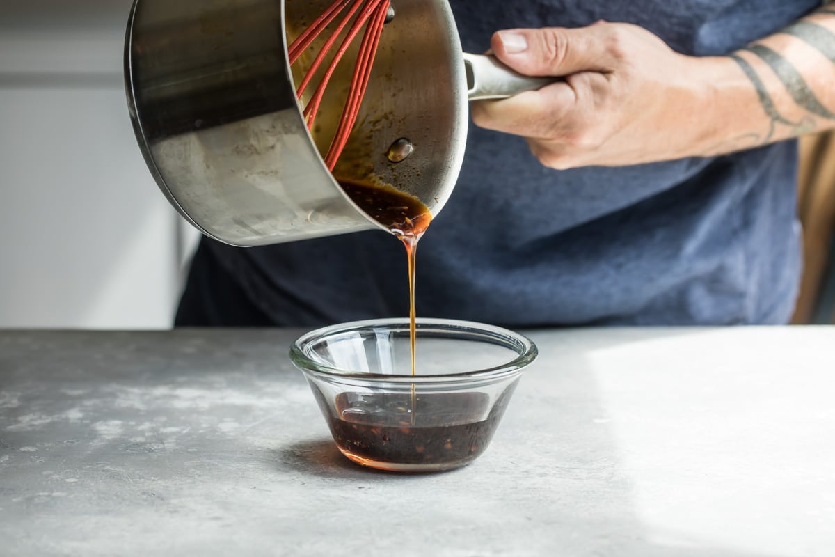 Pouring teriyaki sauce from a saucepan into a glass bowl.