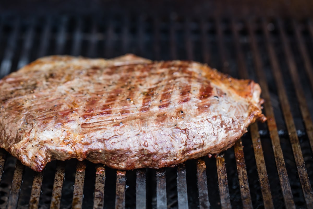 A piece of steak cooking on a grill.