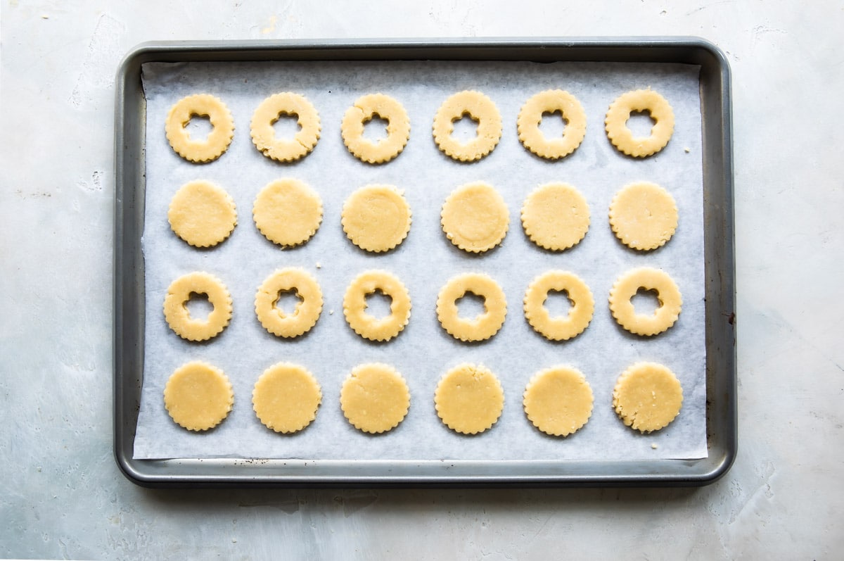 Linzer cookie cut outs on a baking sheet before being baked.