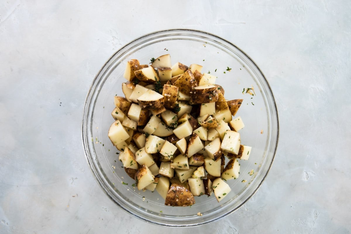 Cubed, raw, potatoes in a bowl with olive oil and seasonings.