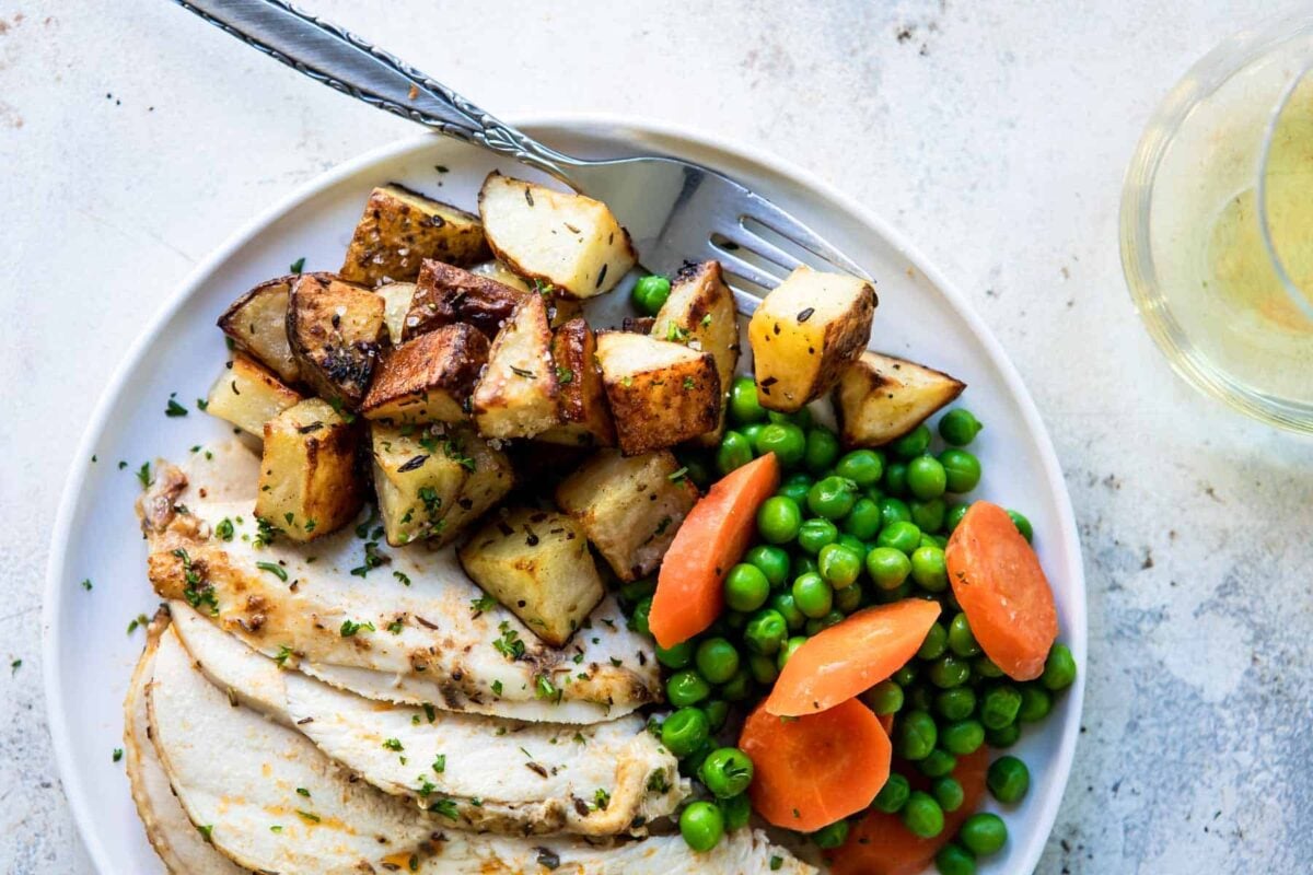 A plate with chicken slices, roasted potatoes, peas and carrots.