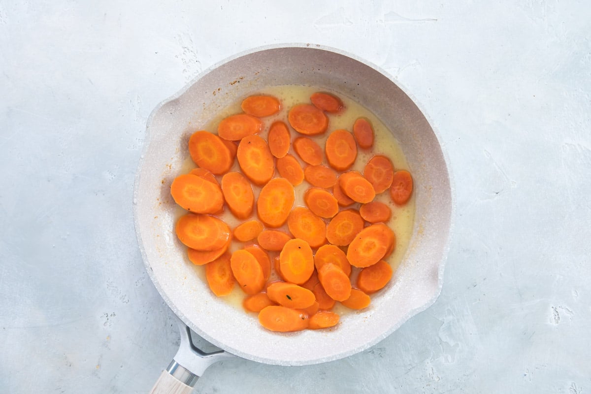 Carrots being cooked in butter in a white pan.