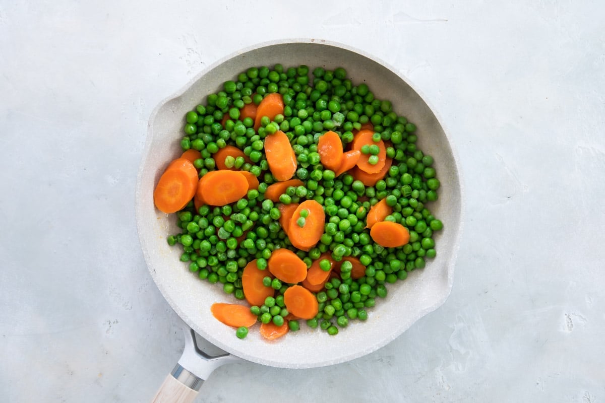 Peas and carrots being cooked in a white pan.
