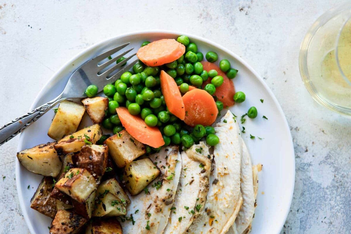 Peas and carrots on a white plate with potato cubes and chicken slices.