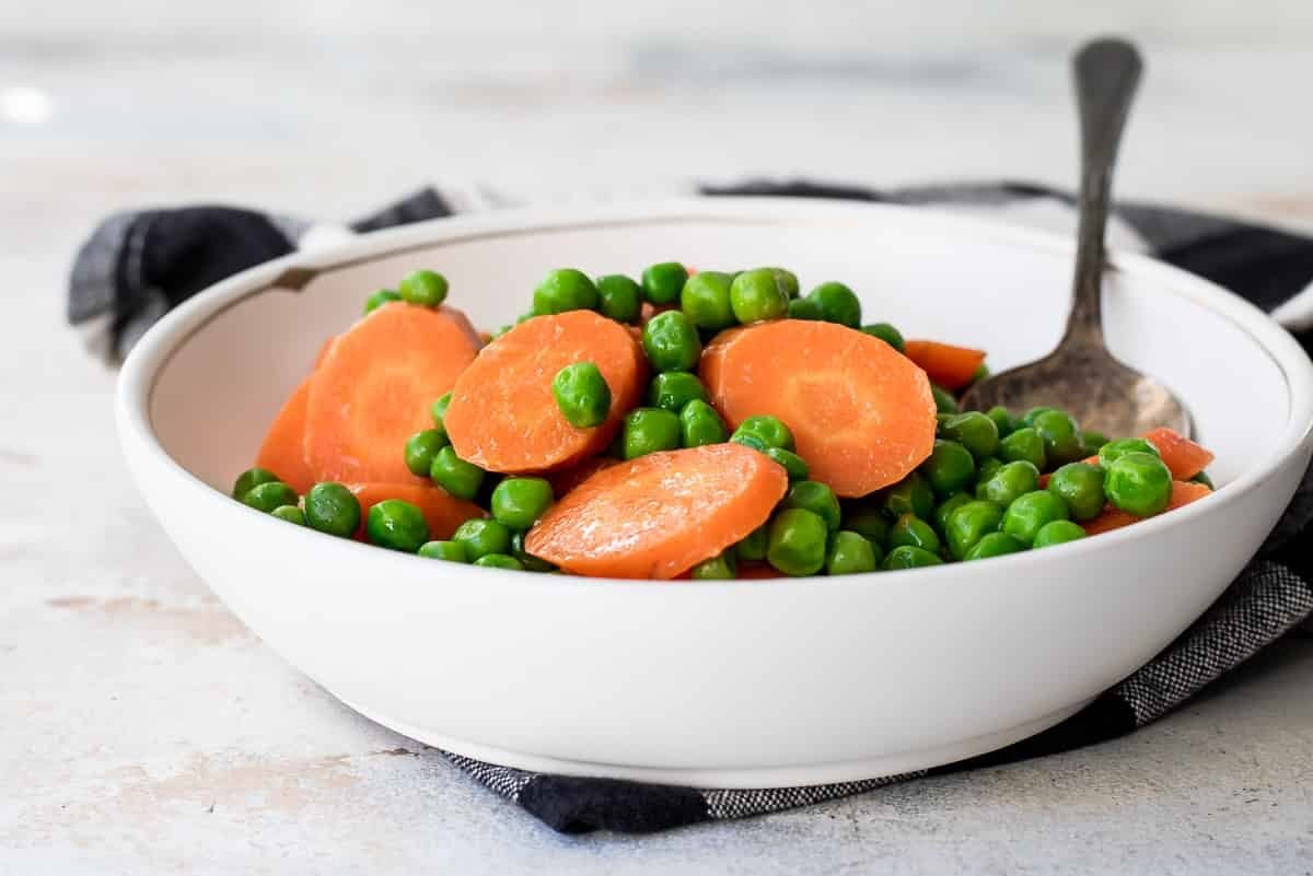 Peas and carrots in a white bowl.
