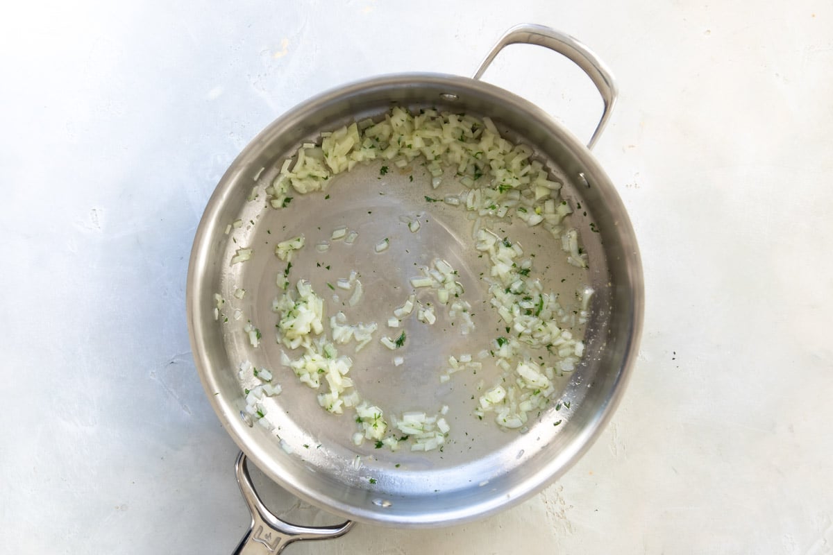 A saucepan with onion and parsley cooking in olive oil.