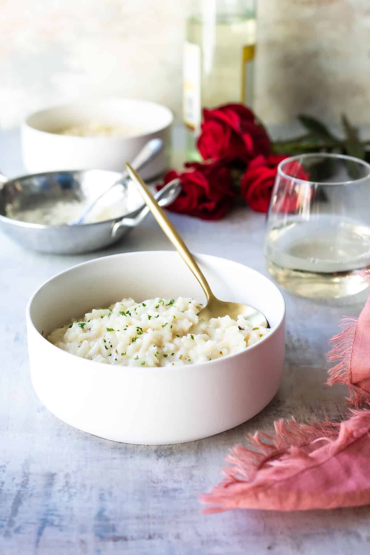 A bowl full of Risotto with red roses and white wine in the background.