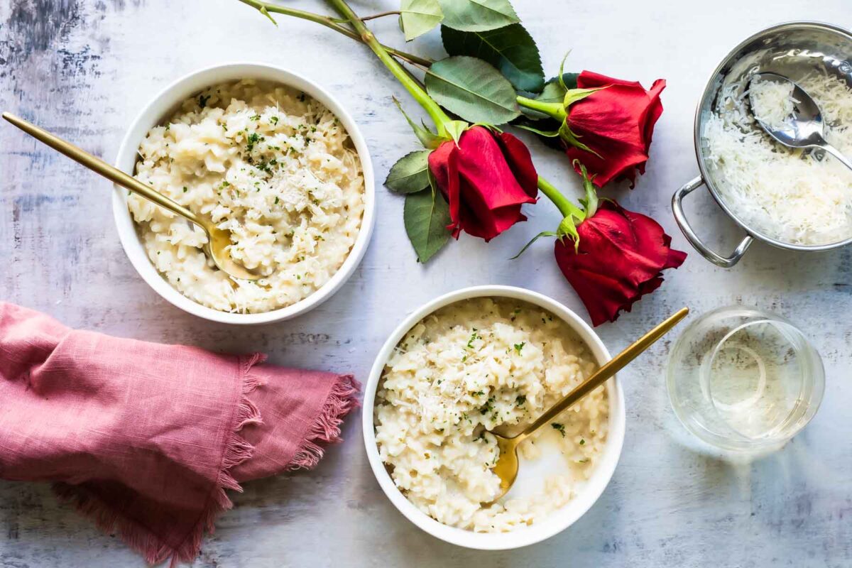 2 bowls full of Risotto with red roses and white wine next to them.