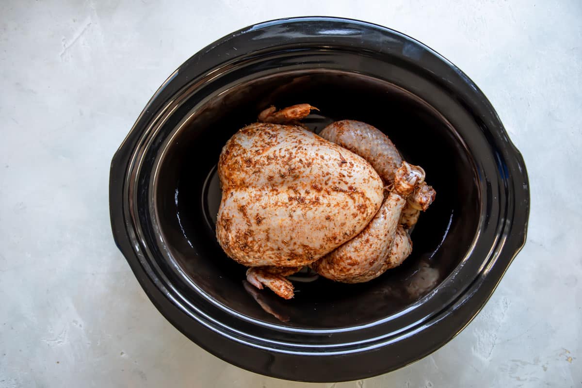 An uncooked rotisserie chicken in a black crock pot.