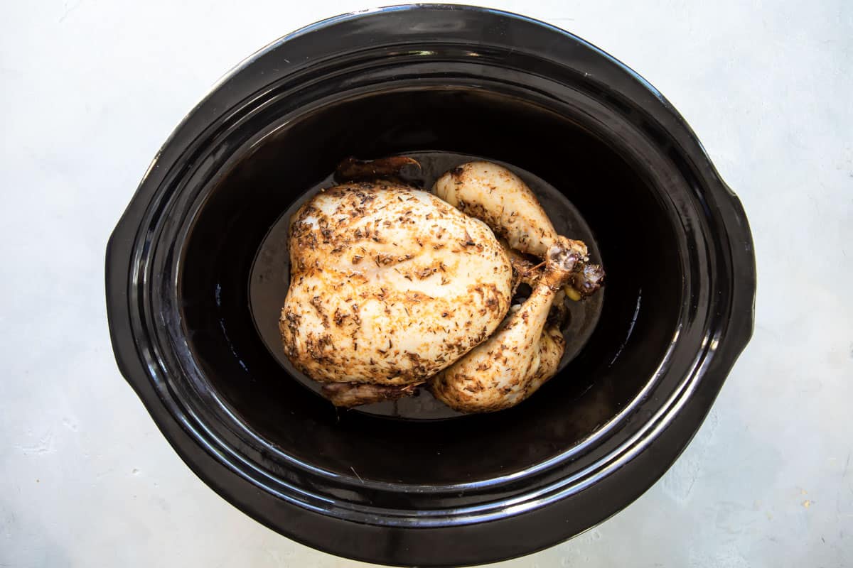 An cooked rotisserie chicken in a black crock pot.