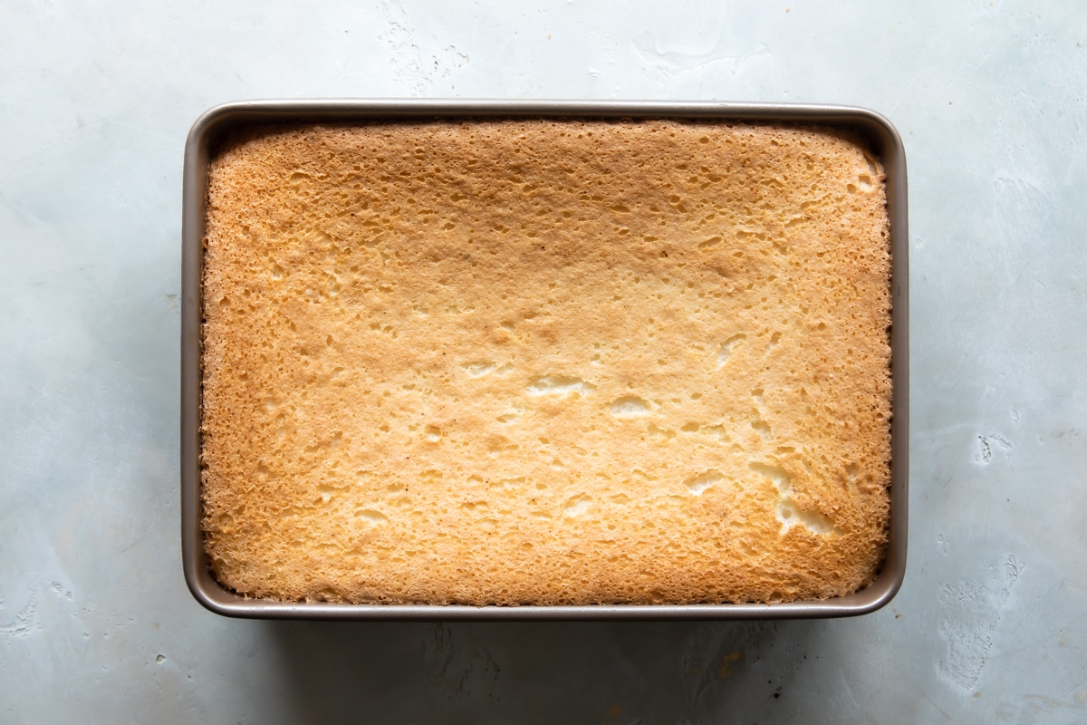 Angel food cake in a rectangular pan for jello poke cake.