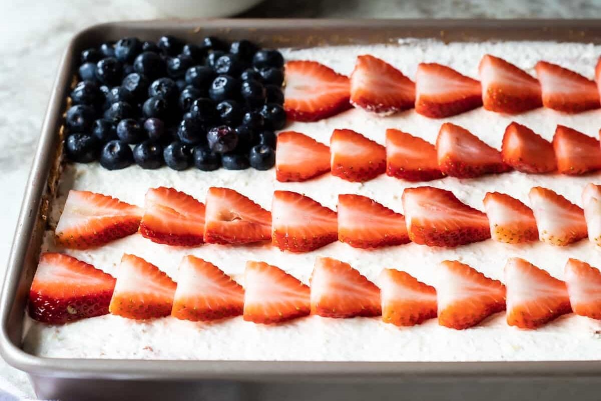 Strawberry jello poke cake topped with strawberries and blueberries to look like an American flag.