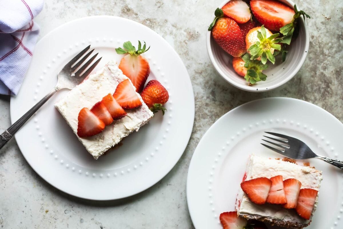 Two slices of strawberry jello poke cake on white plates.